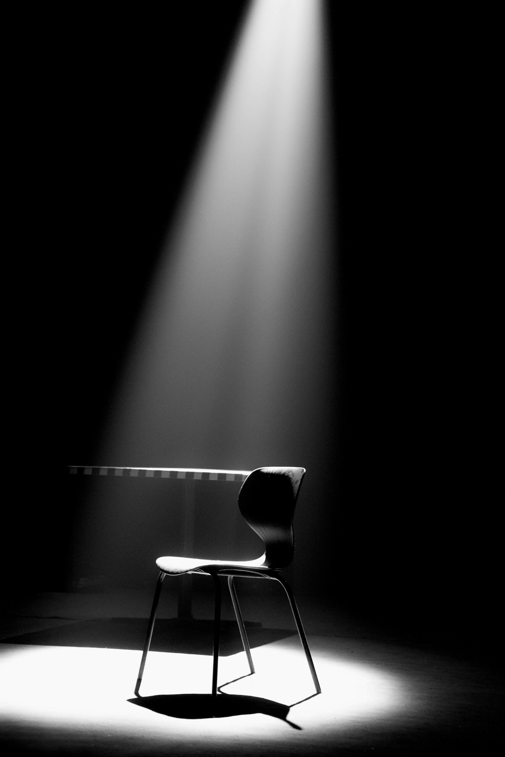 A single empty chair under a hard spotlight on a dark stage