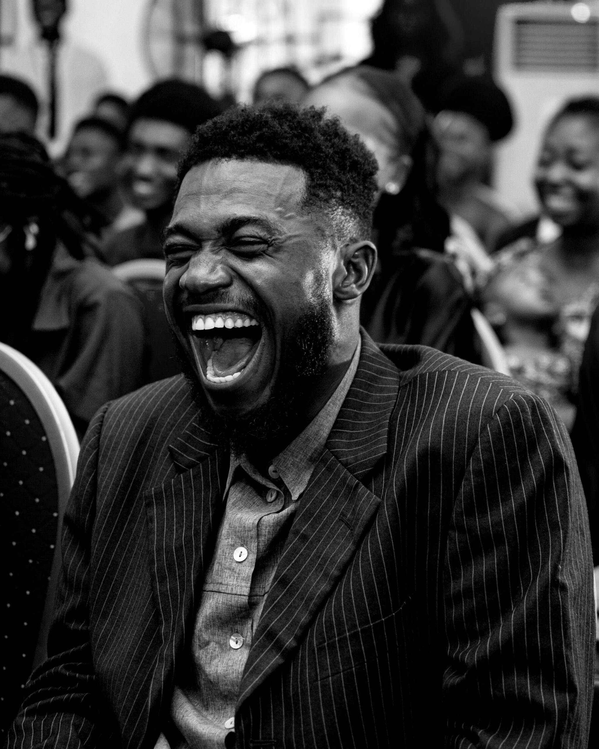 A man in a pinstripe suit laughing helplessly in the middle of an audience